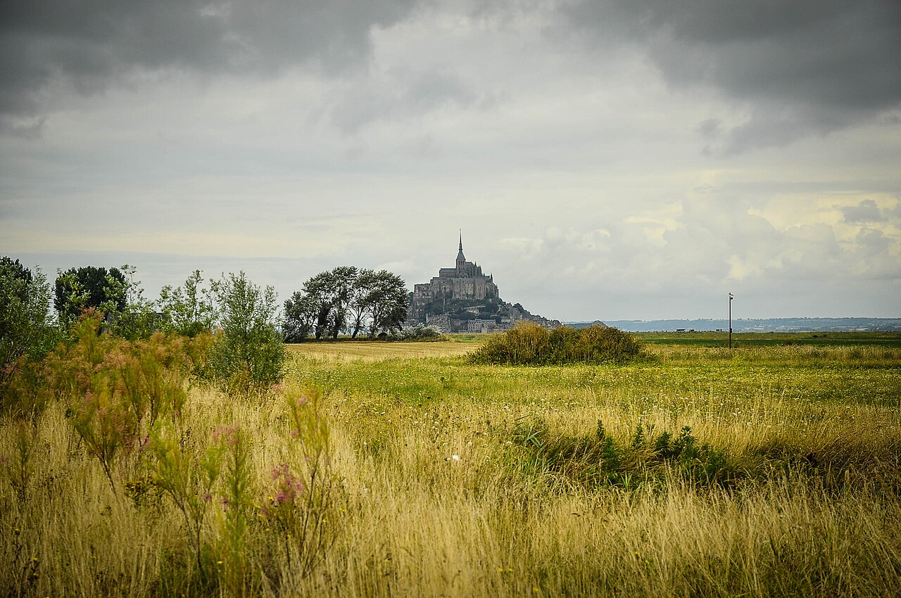 Mont-Saint-Michel is completely surrounded by water, with part of the footbridge submerged and tourists standing in a safe area in the distance. This confirms the official description that the island reappears when the tidal coefficient exceeds 110, helping travelers understand the visual impact of the 'island moment.'