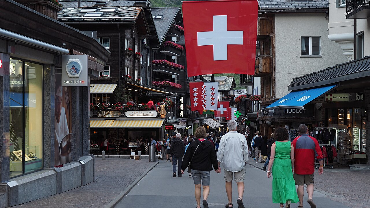 Zermatt's main street with Swiss flags, lined with shops and wooden chalets