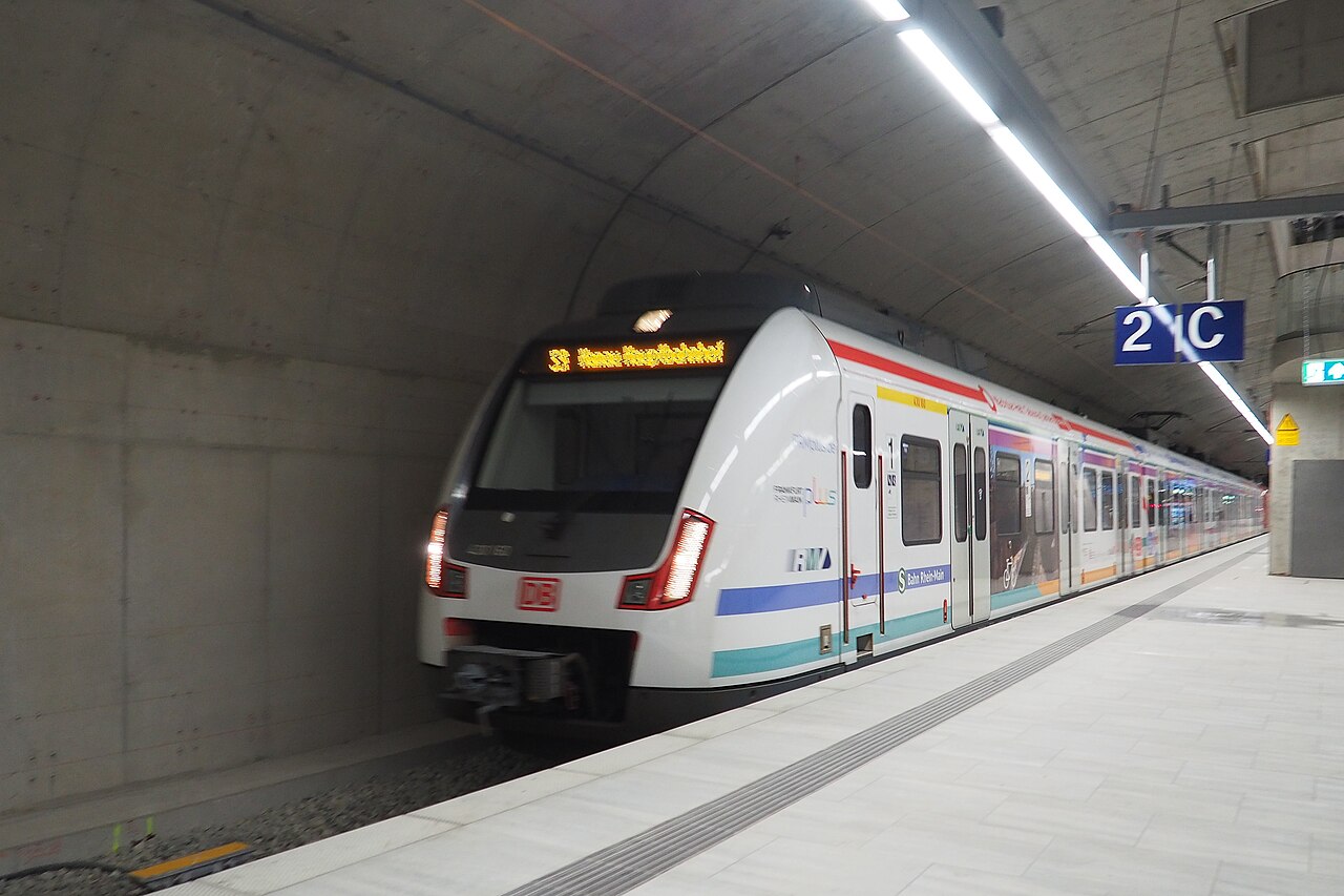 Frankfurt的地铁站台内,一列S - Bahn列车停靠在标有“2/C”的站台,车头电子屏显示“33 Hanau Hauptbahnhof”,站台墙面为混凝土材质,地面铺白色地砖,上方有长条形灯光照明,右侧有蓝色“2/C”站台标识。