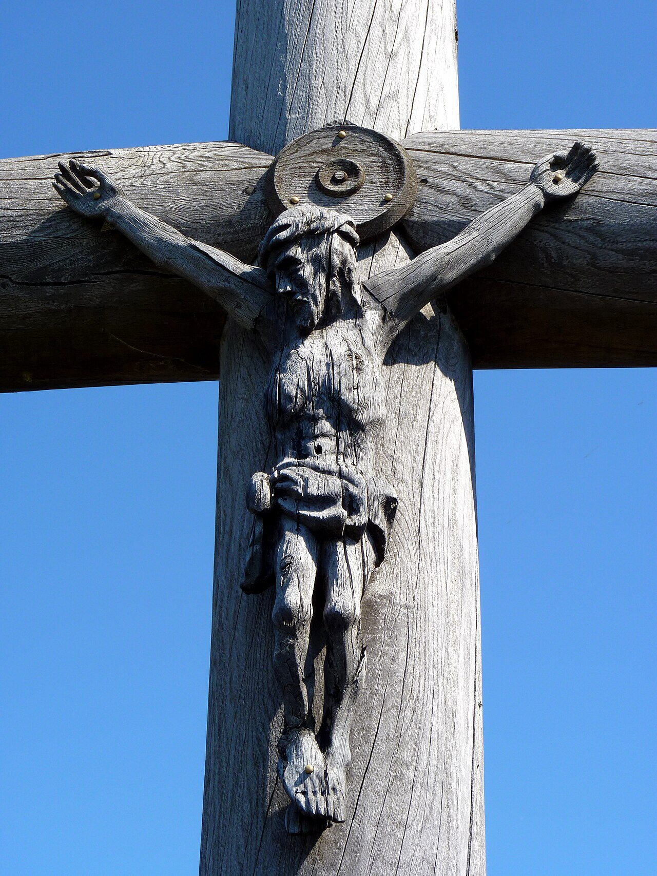 Close-up of a grey weathered wooden crucifix on the Hill of Crosses against a blue sky