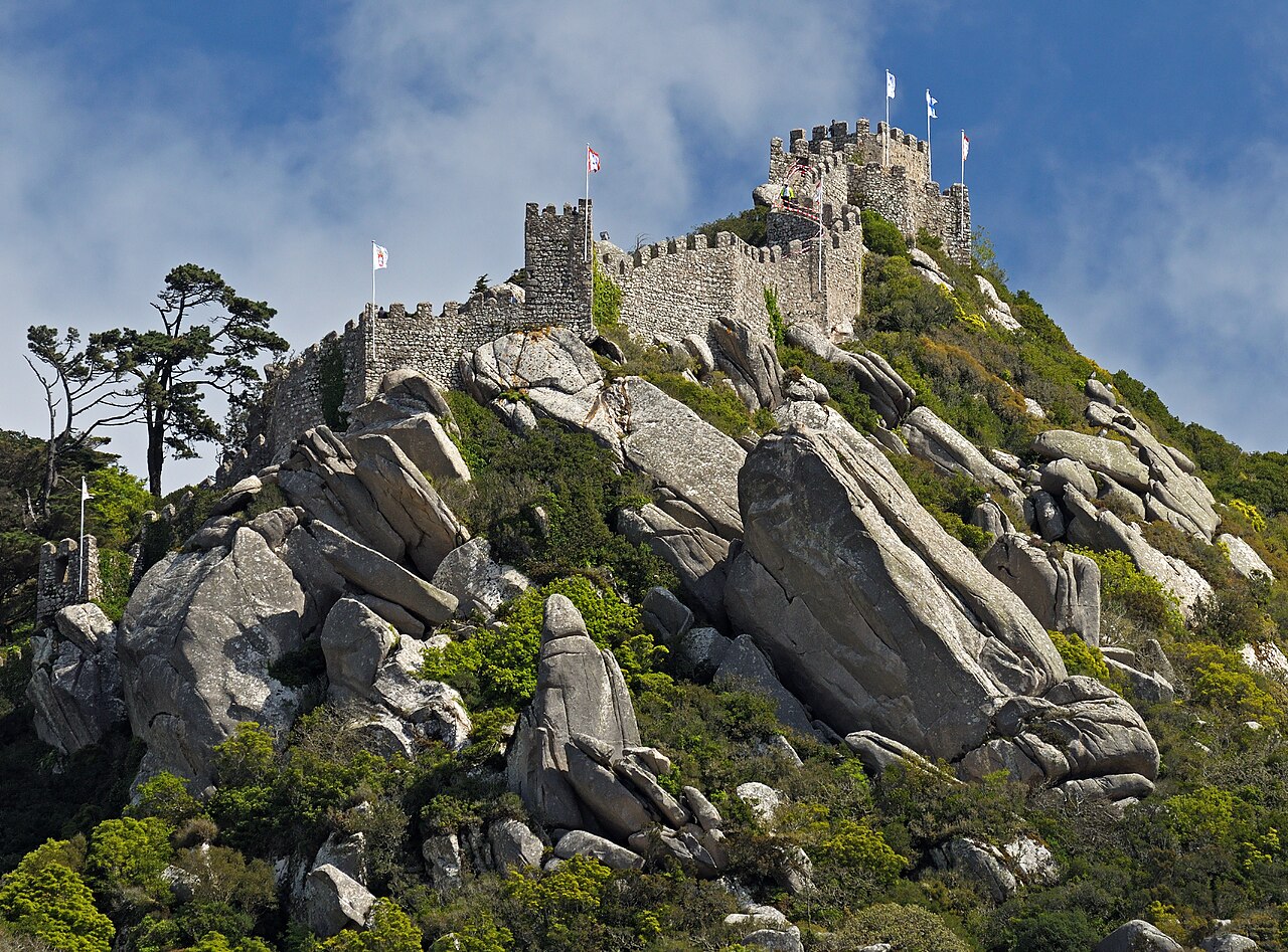The crenellated walls of the Moorish Castle snake along the ridge—sharing the same ridge as the Pena Palace, with uphill transport linked by the 434 loop, often visited together.