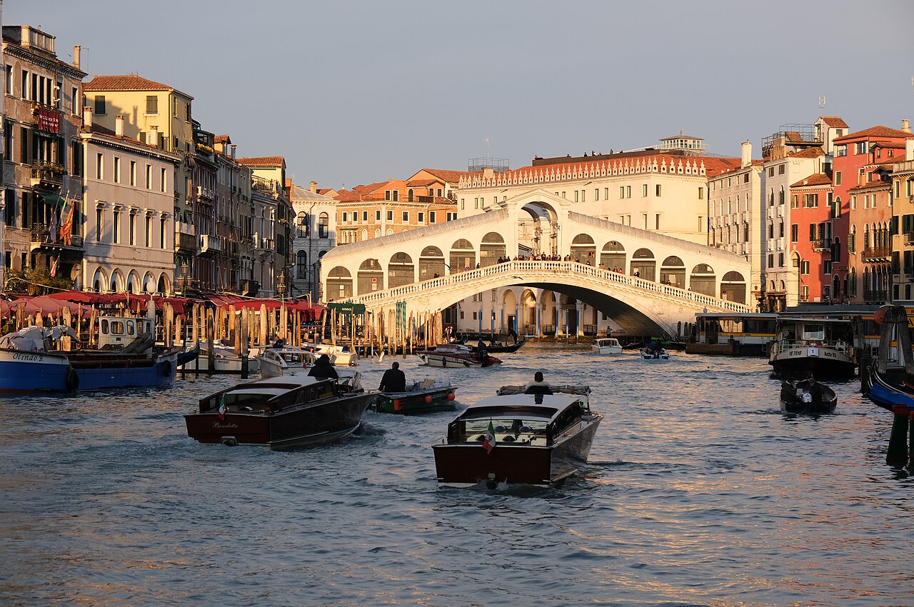 Grand Canal under Rialto Bridge: water taxis and vaporettos are Venice's entire 'traffic' — the final leg from airport or station to your accommodation is all on water, so book it in advance if you're carrying luggage.