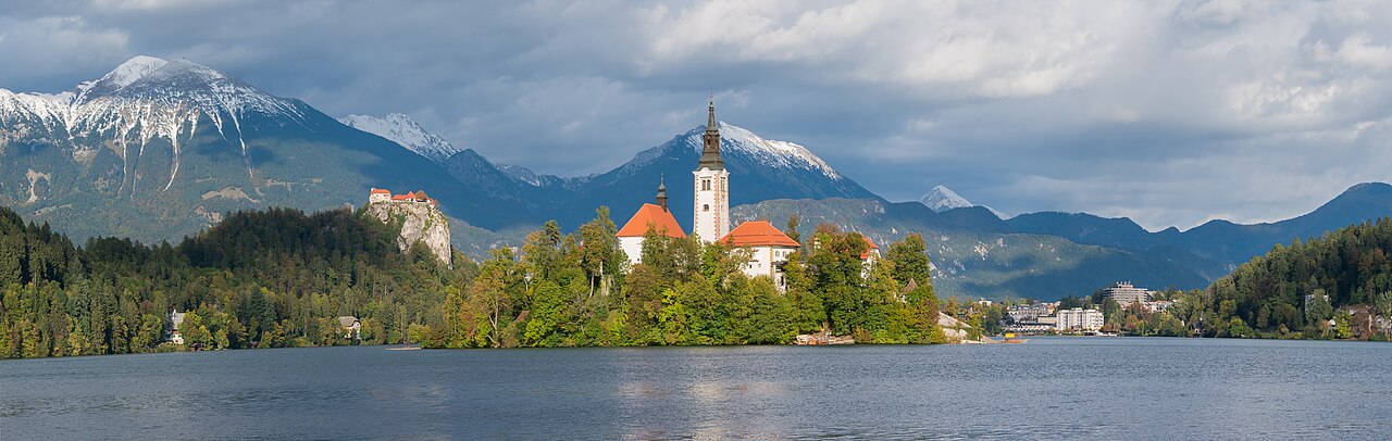 Lake Bled island church bell tower and Bled Castle on the cliff in the distance, with snowy mountains in the background
