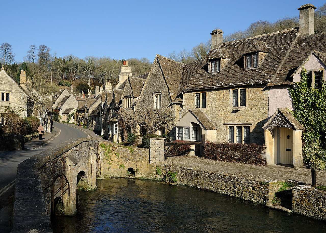 Castle Combe in the Cotswolds: honey-coloured limestone cottages along a street, with an old low stone bridge over the brook in the foreground