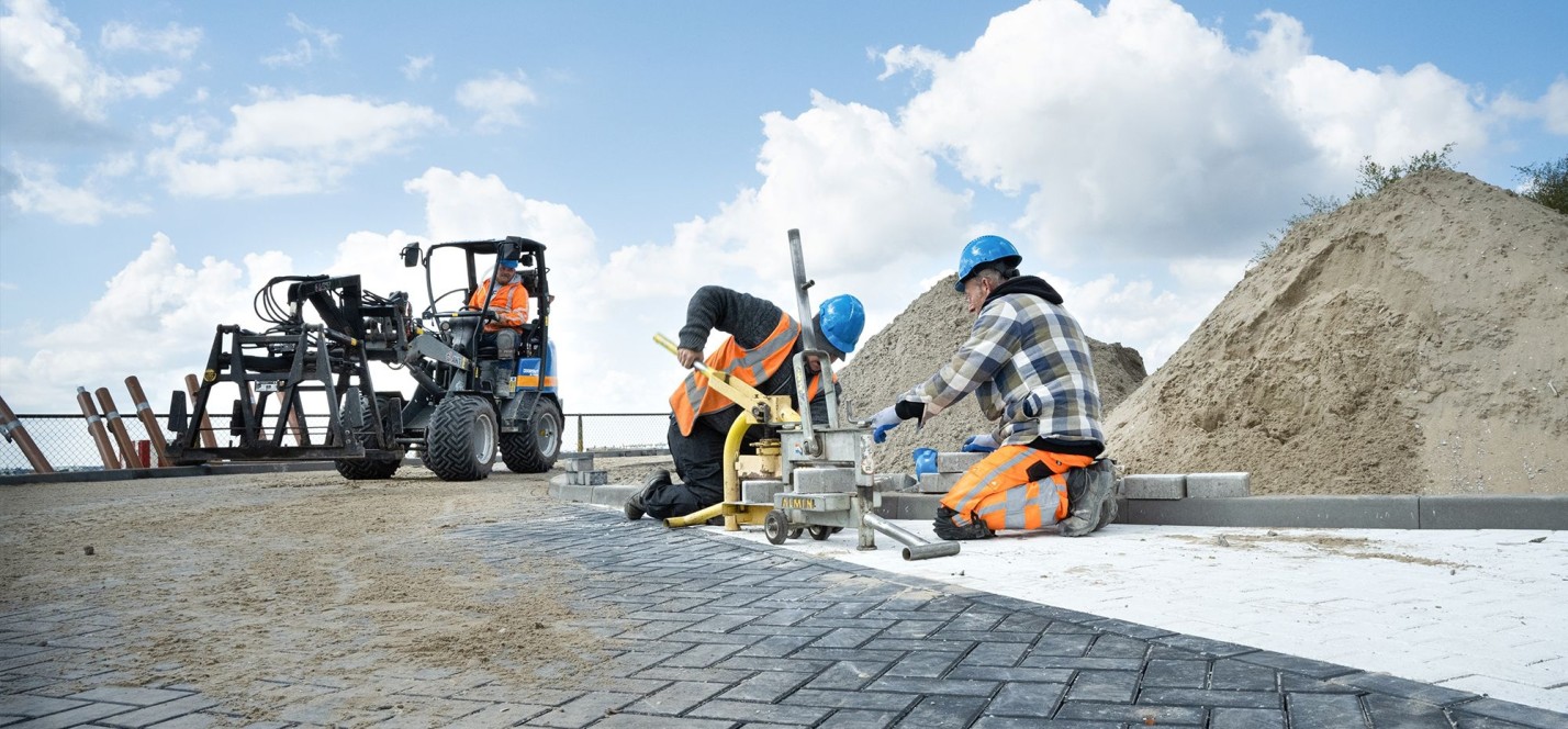 Man aan het straten en iemand die een shovel bestuurt