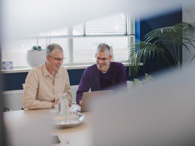 Dennis en Roy achter een laptop in een spreekruimte