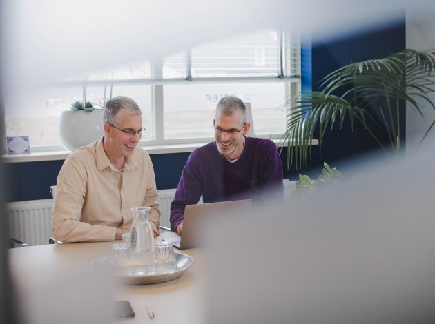 Dennis en Roy achter een laptop in een spreekruimte