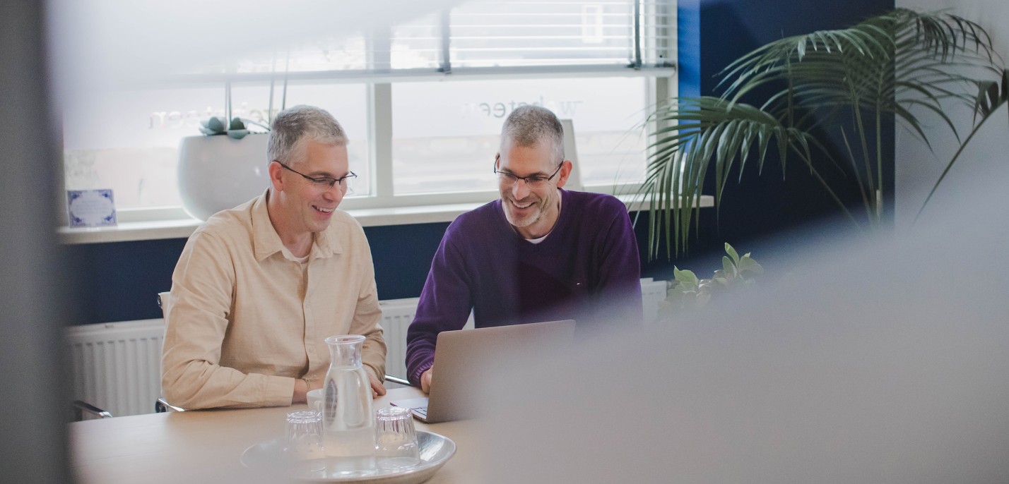 Dennis en Roy achter een laptop in een spreekruimte