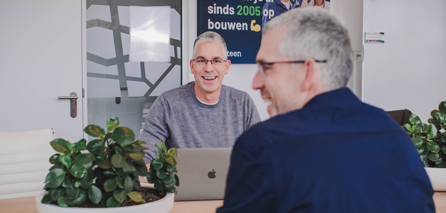 Dennis en Roy achter een laptop in een spreekruimte