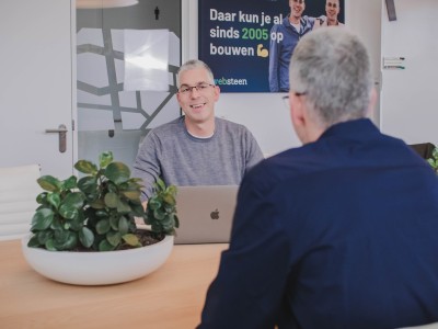 Roy glimlacht terwijl hij met iemand praat in een spreekruimte