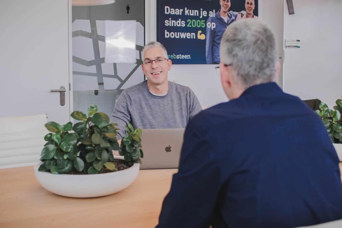 Roy glimlacht terwijl hij met iemand praat in een spreekruimte