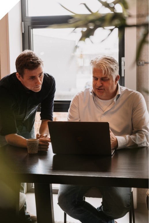 Twee ondernemers bespreken financiële cijfers op een laptop aan tafel in een kantooromgeving, als voorbeeld van zakelijk financieel advies voor MKB en zzp’ers.