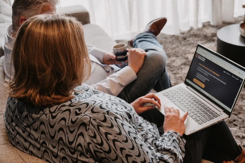 Vrouw met halflang haar werkt op een laptop; naast haar zit een man met een kop koffie, gedeeltelijk zichtbaar.