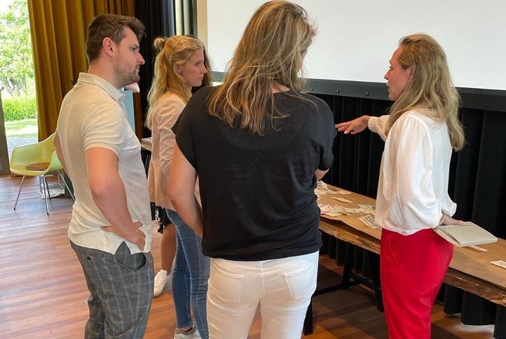 Stefanie in gesprek met 2 jonge dames en 1 heer. De setting is een ruimte voor brainstorm. op de tafel liggen flipoverpapieren en post-its