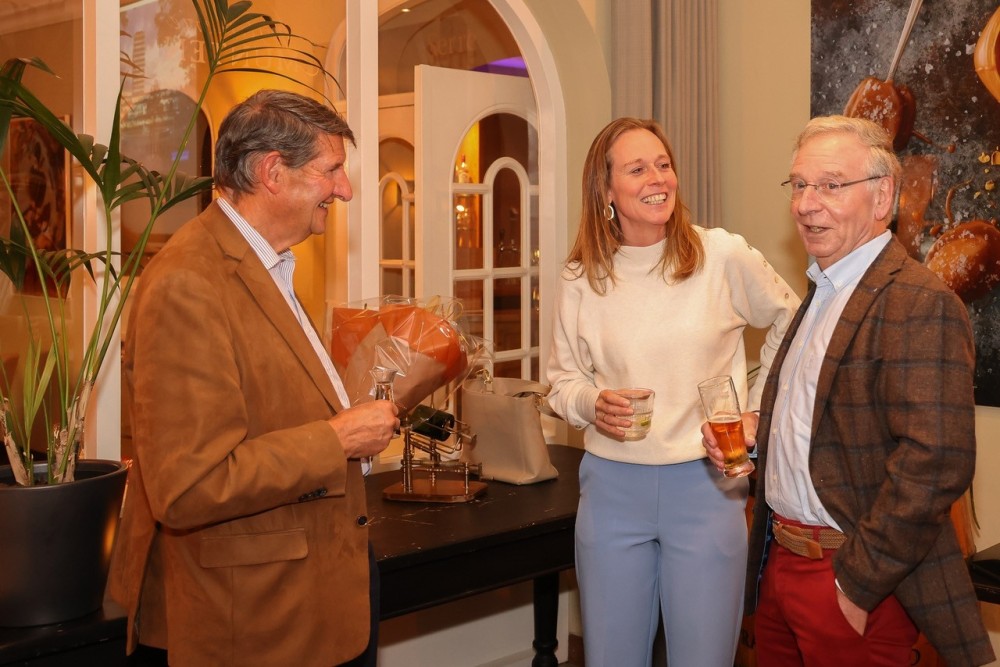 Stefanie in gesprek met twee keurig geklede heren op leeftijd in een horecagelegenheid