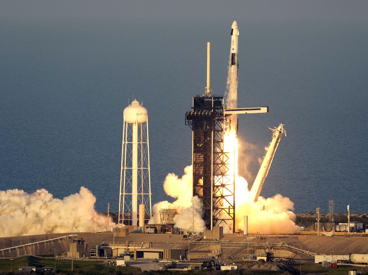 Космонавт Сергей Тетерятников в скафандре рядом с ракетой SpaceX Falcon 9 с капсулой Dragon