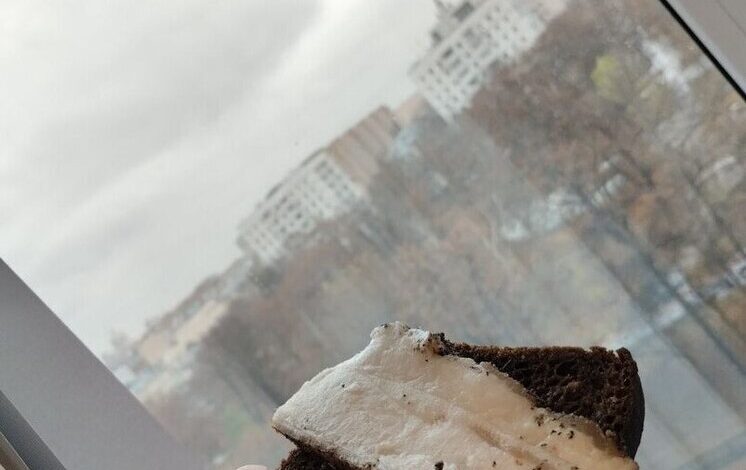 Крупный план куска сала на разделочной доске, рядом нож и специи. На заднем плане размытый интерьер кухни.