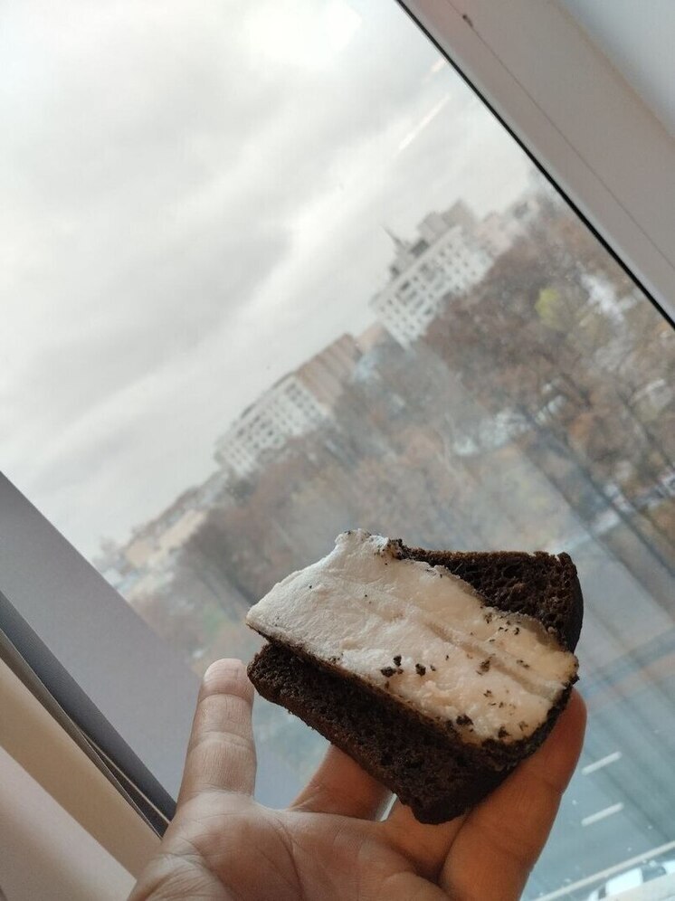 Крупный план куска сала на разделочной доске, рядом нож и специи. На заднем плане размытый интерьер кухни.