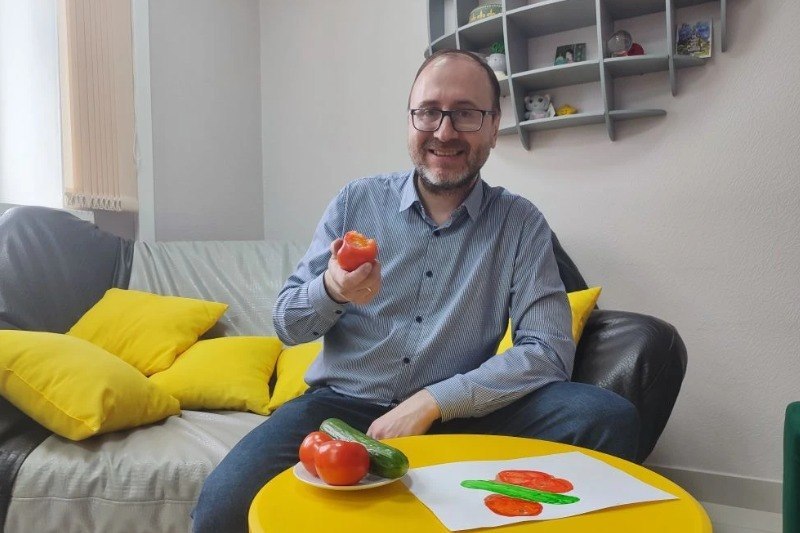 Человек лежит на диване, расслабленный, с улыбкой, рядом тарелка с пельменями.