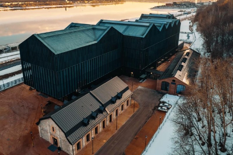 Группа людей в костюмах, напоминающих образы древних богов, отмечает новоселье в современном арт-пространстве, демонстрируя смешение традиций и современности.