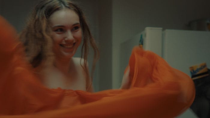 Behind the Pose (2025) Still — Masha with Orange Dress