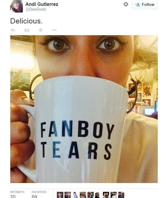 Женщина держит кружку с надписью 'FANBOY TEARS' и улыбается в камеру.