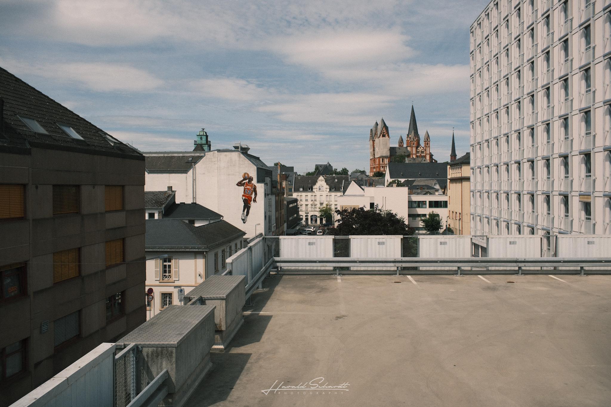 View from the top level of a parking garage toward Limburg Cathedral, with rooftops and modern buildings in the foreground.