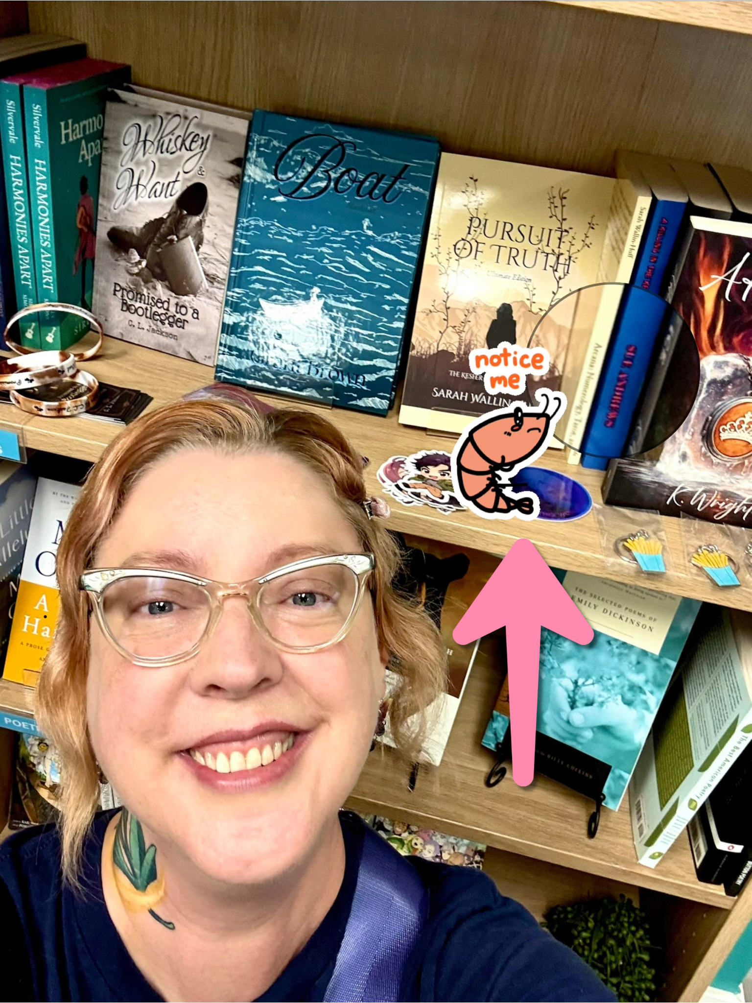 A selfie in front of a bookstore shelf displaying various books, including one titled "Pursuit of Truth" by Sarah Wallin-Huff. A pink arrow and a cartoon shrimp sticker with the words "notice me" point toward the books.