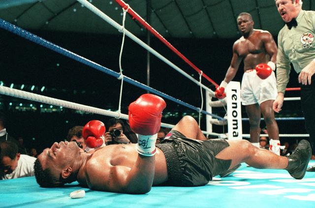 Boxing ring scene with a knocked-down boxer (Mike Tyson) lying on the canvas while the referee and opponent stand nearby.