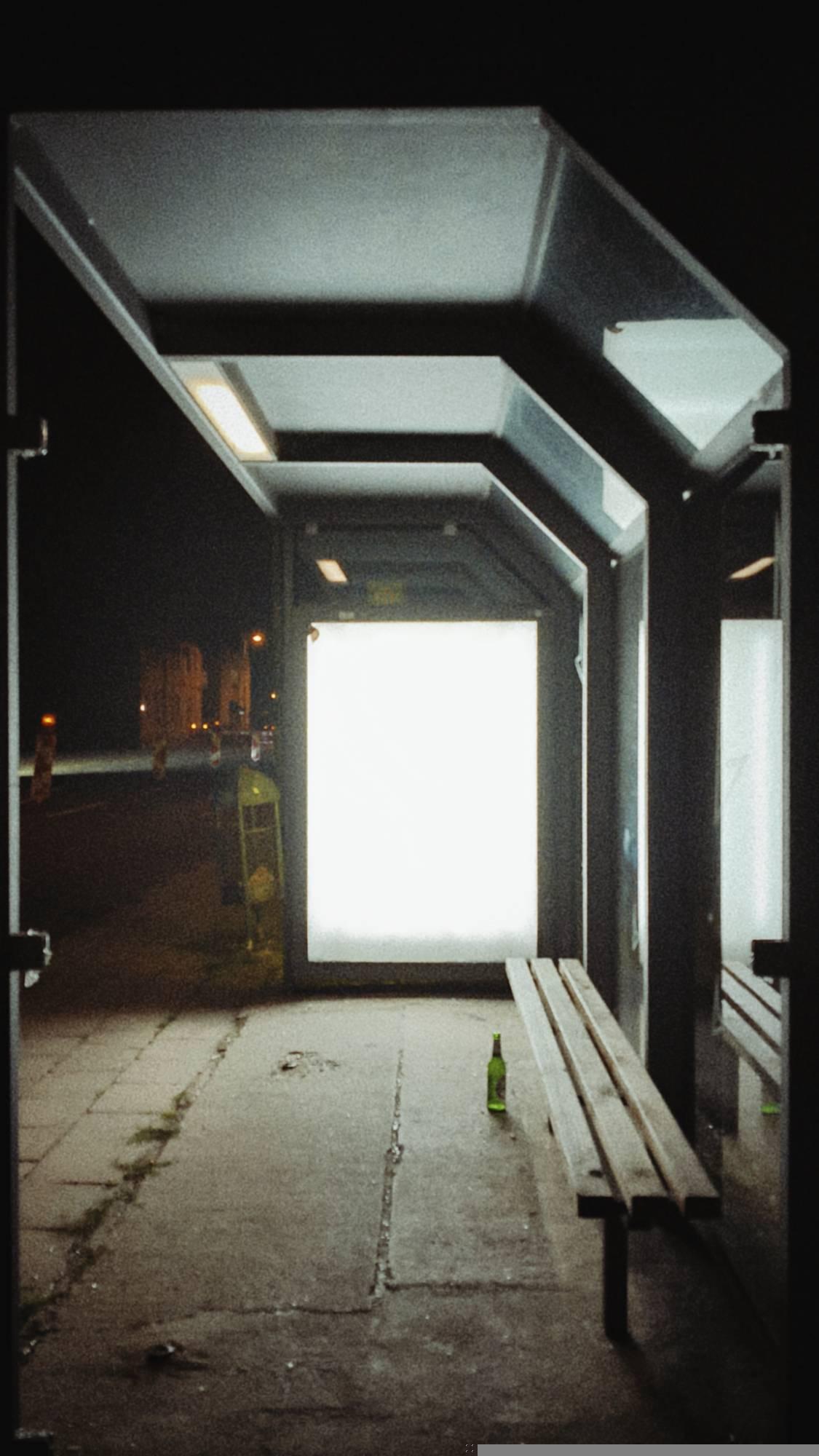 An empty bus stop. An empty white advertising panel. An empty bottle of beer.