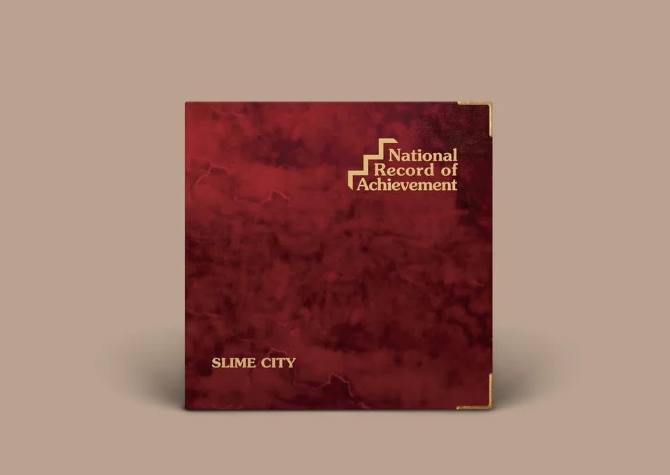 A photograph of a vinyl LP sleeve. It shows a mottled red/black design with the old late-nineties ‘National Record of Achievement’ logo in the top right and ‘Slime City’ in gold on the bottom right.