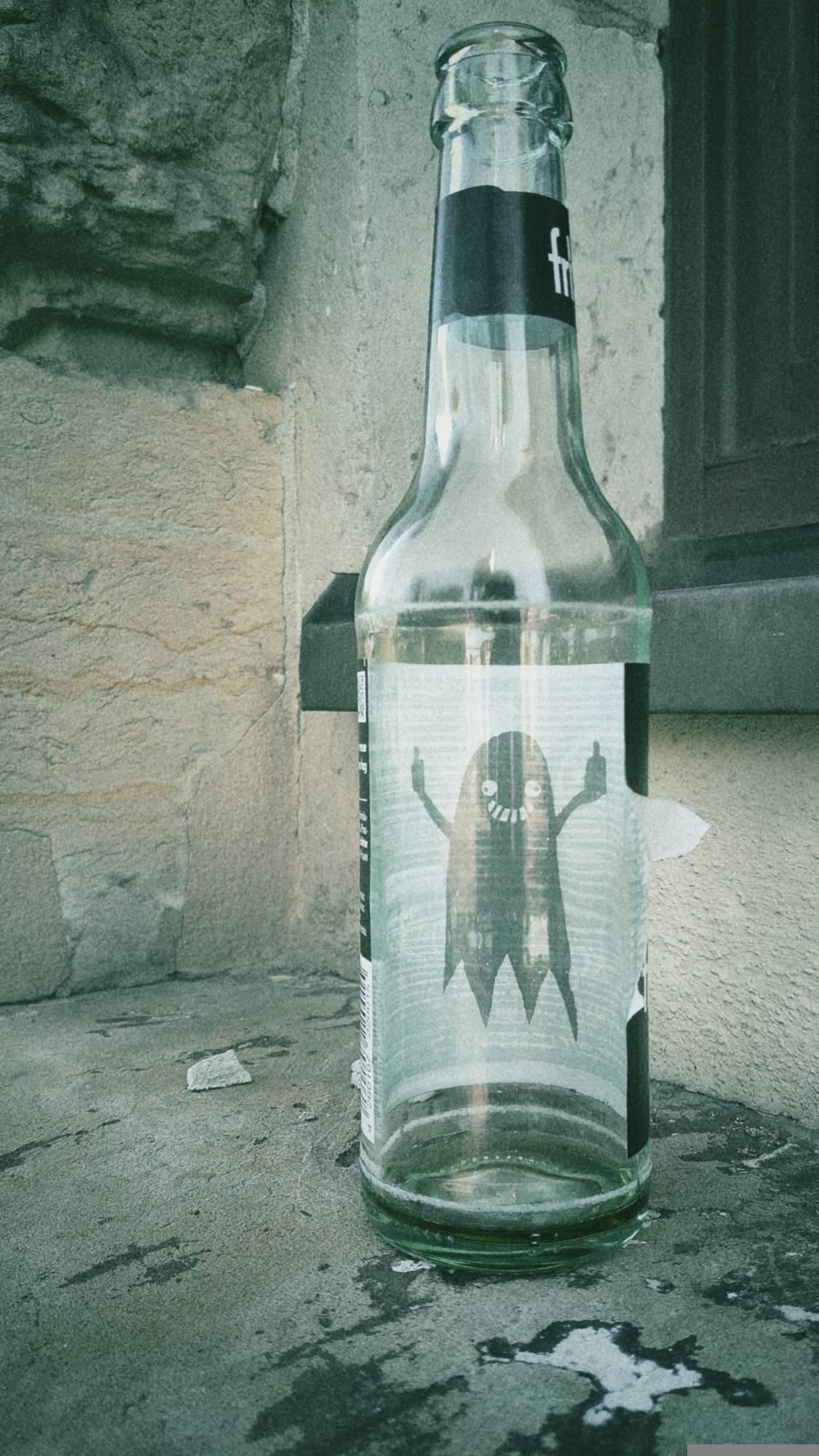An empty Fritz Cola bottle on an old windowsill. The inner side of the label is white and has a black ghost on it. The ghost is grinning wide and has two middle fingers up.