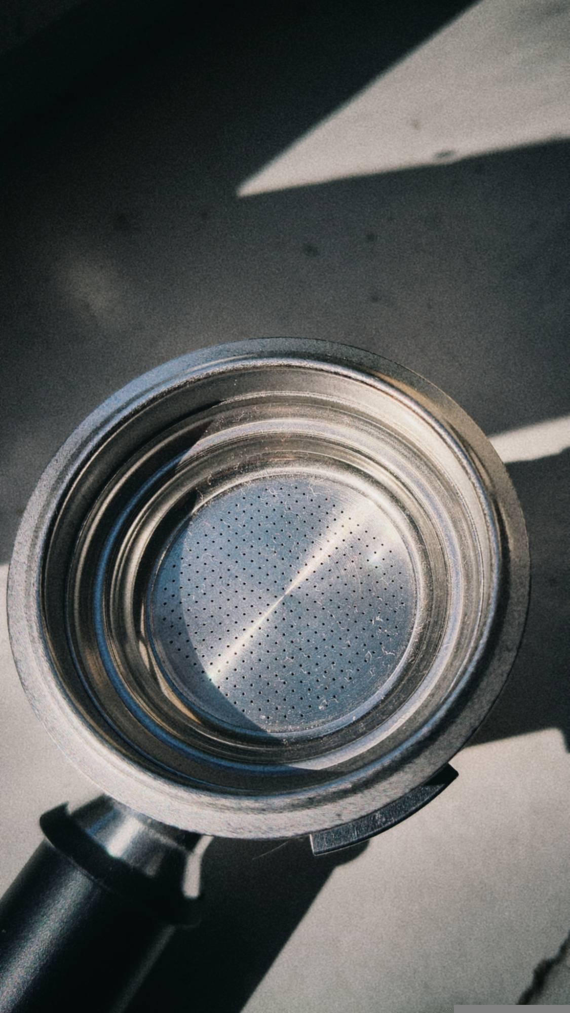 Part of a coffee maker on a white wooden board in bright sunlight.