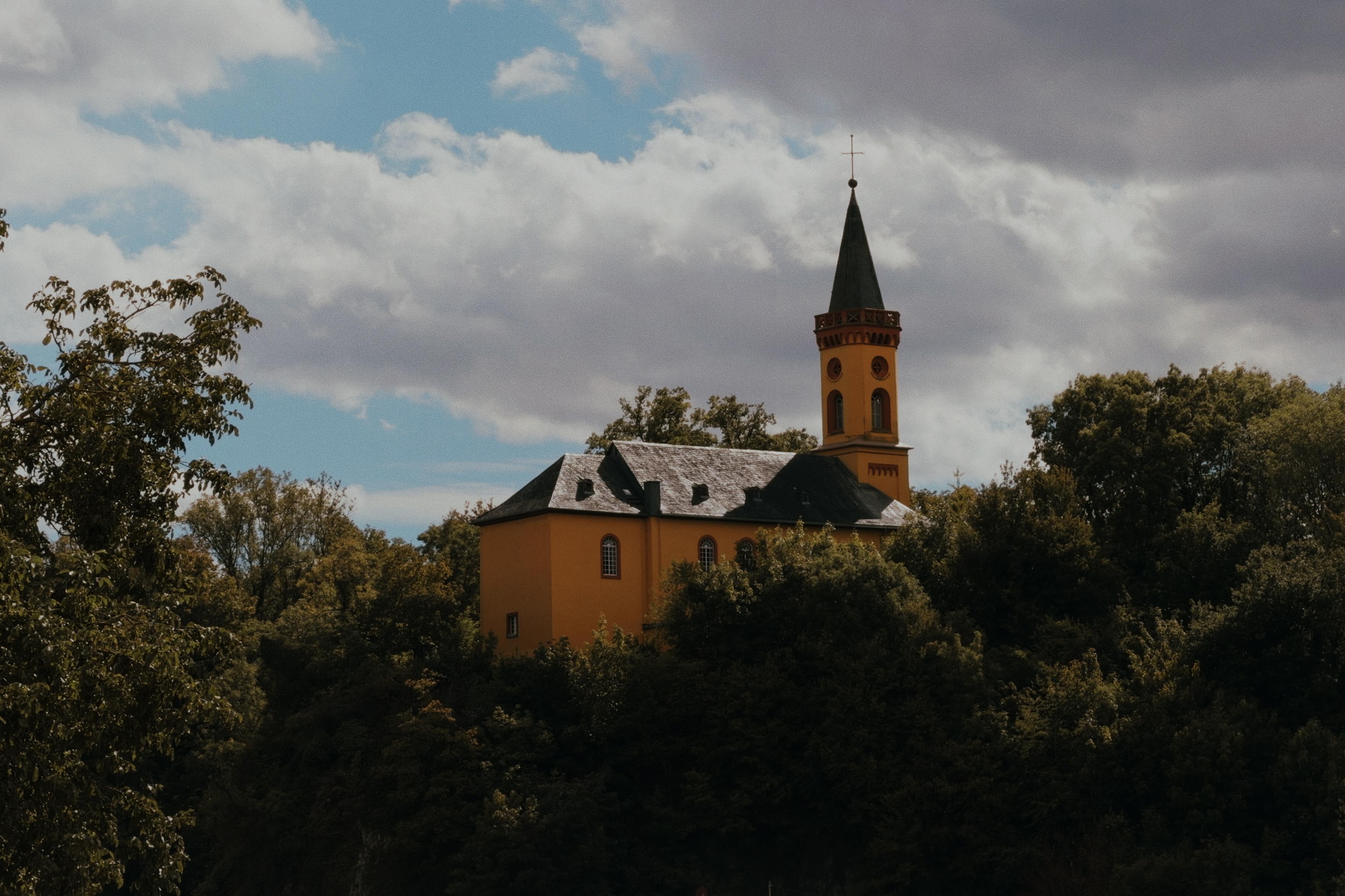 Yellow church rising above the trees beneath a partly cloudy sky.