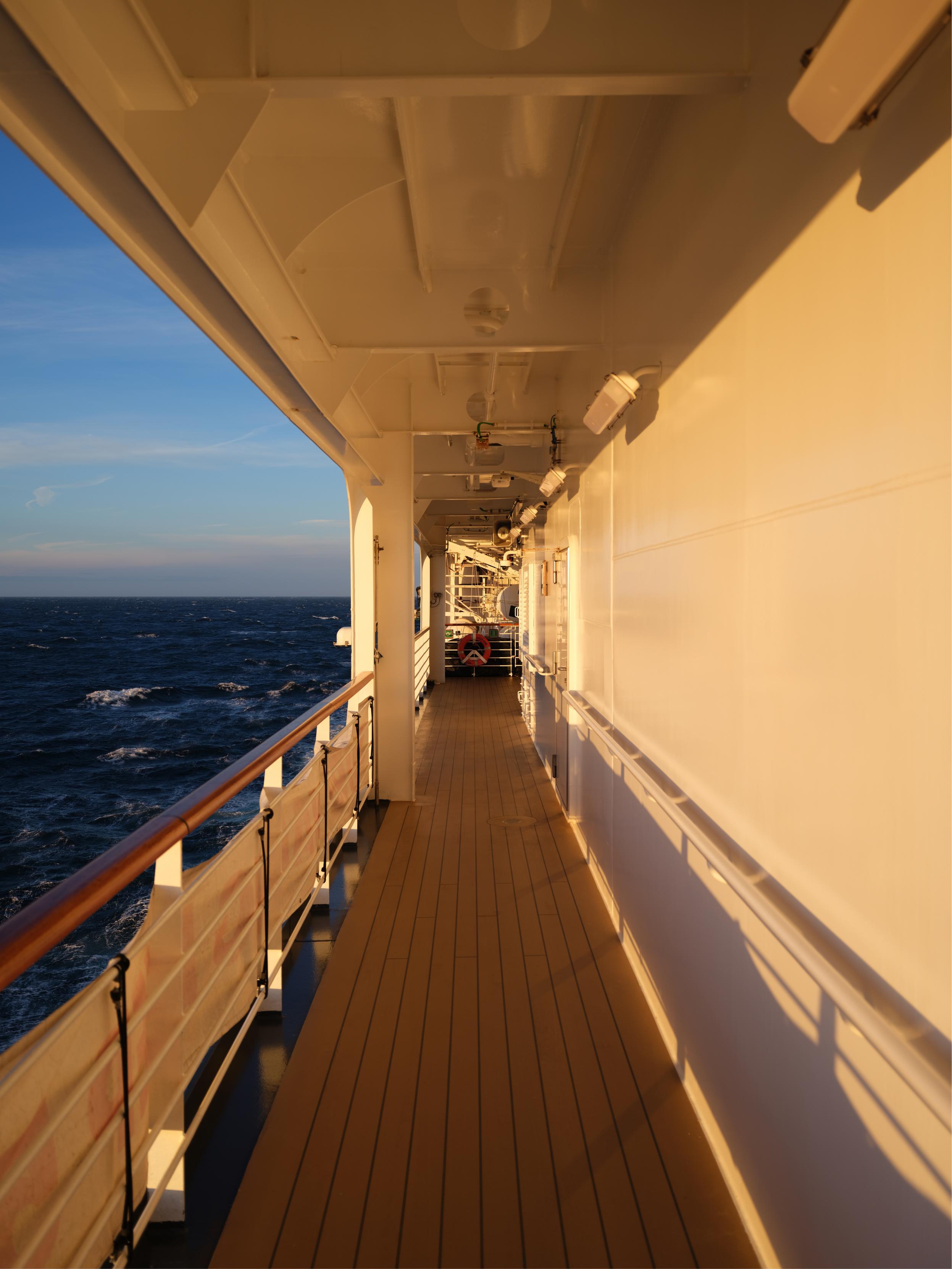 A wooden walkway with white walls and a metal railing, with the ocean in the background.