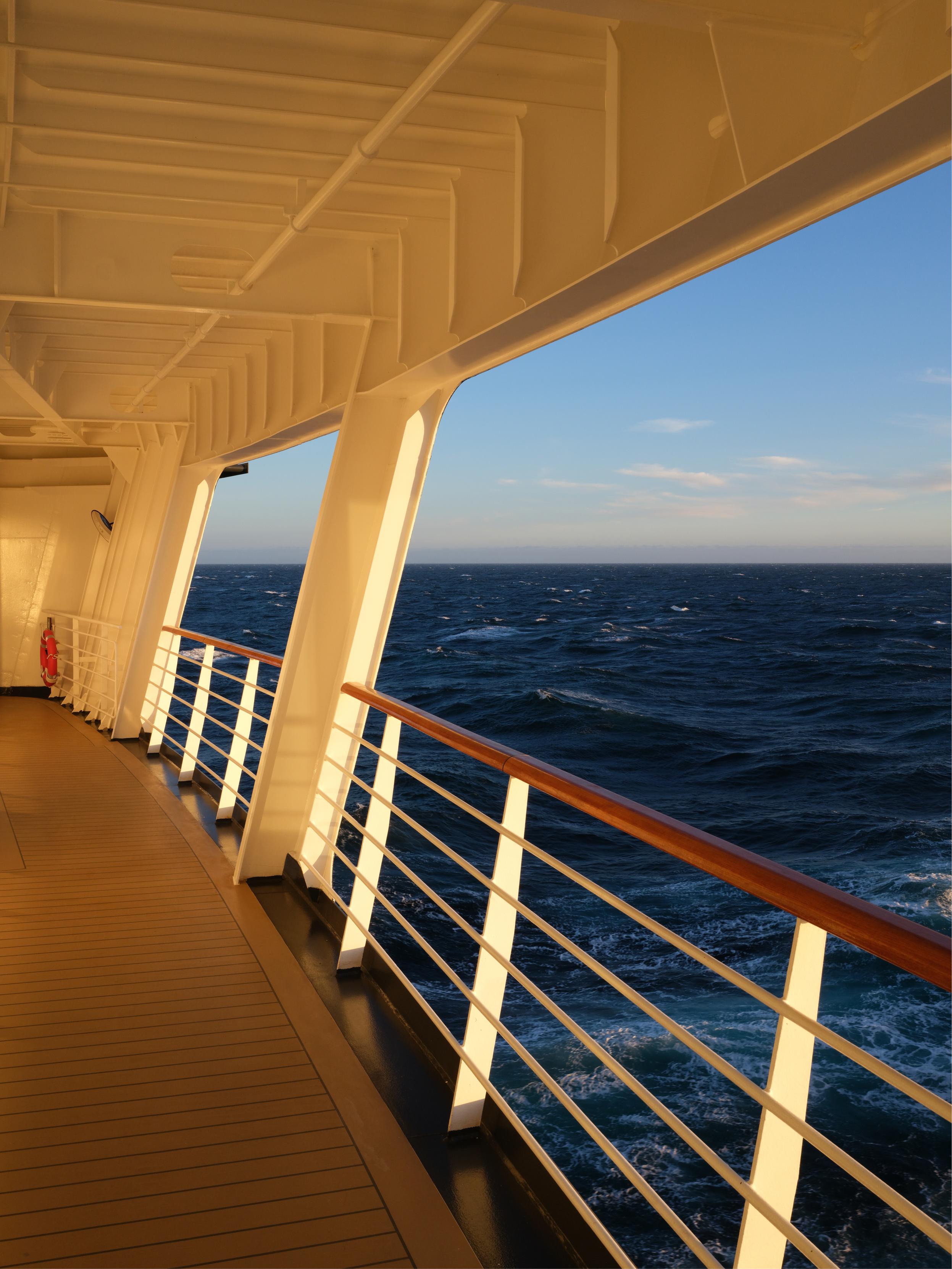 A wooden walkway with a metal railing overlooking a blue sea under a clear sky.